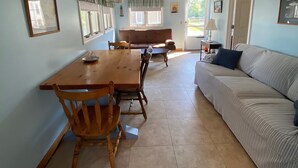A spacious living room with a wooden dining table, two wooden chairs, a sofa, and a bench.