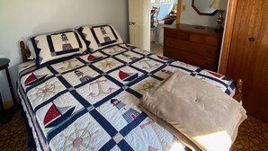 A bedroom with a large bed, a wooden dresser, a mirror, and a door leading to another room.