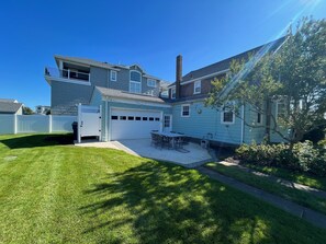 Two-story house with a garage and covered patio area, surrounded by a well-maintained lawn and white fence.