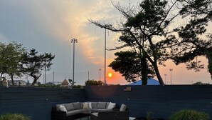 A landscaped outdoor area with a sectional sofa, a small table, and a flag on a wall. - Ocean Ave 5BR: Huge Fenced Yard, Pet Friendly, 2 Houses to Beach + Shark Park! (Brigantine)