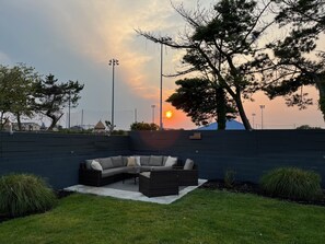 Relax in a serene outdoor seating area with a curved sofa and small table, surrounded by a grassy lawn and a low wall.