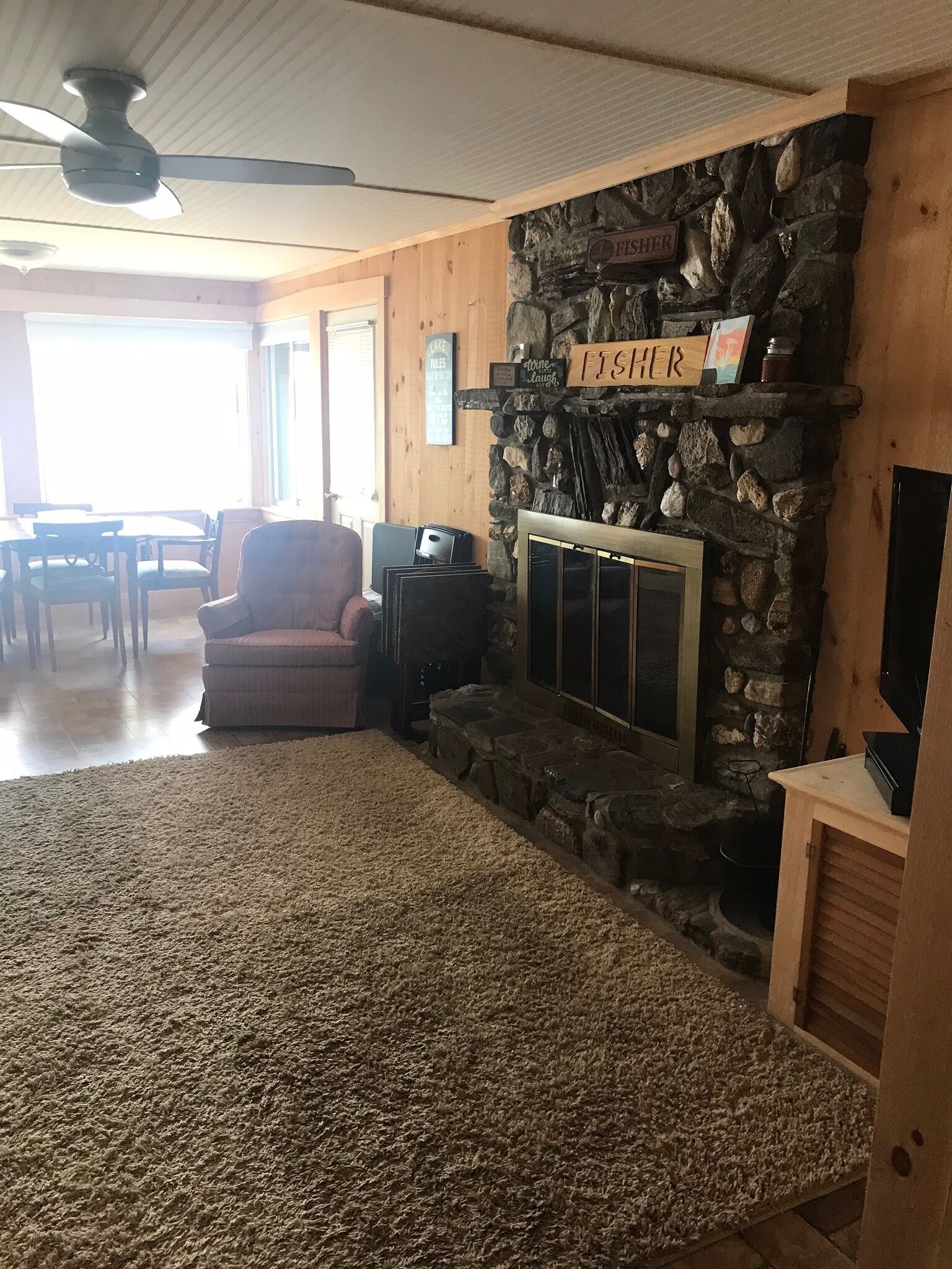 A cozy living room with a stone fireplace, a comfortable armchair, and a television on a wooden stand.