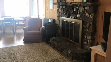 A cozy living room with a stone fireplace, a comfortable armchair, and a television on a wooden stand.