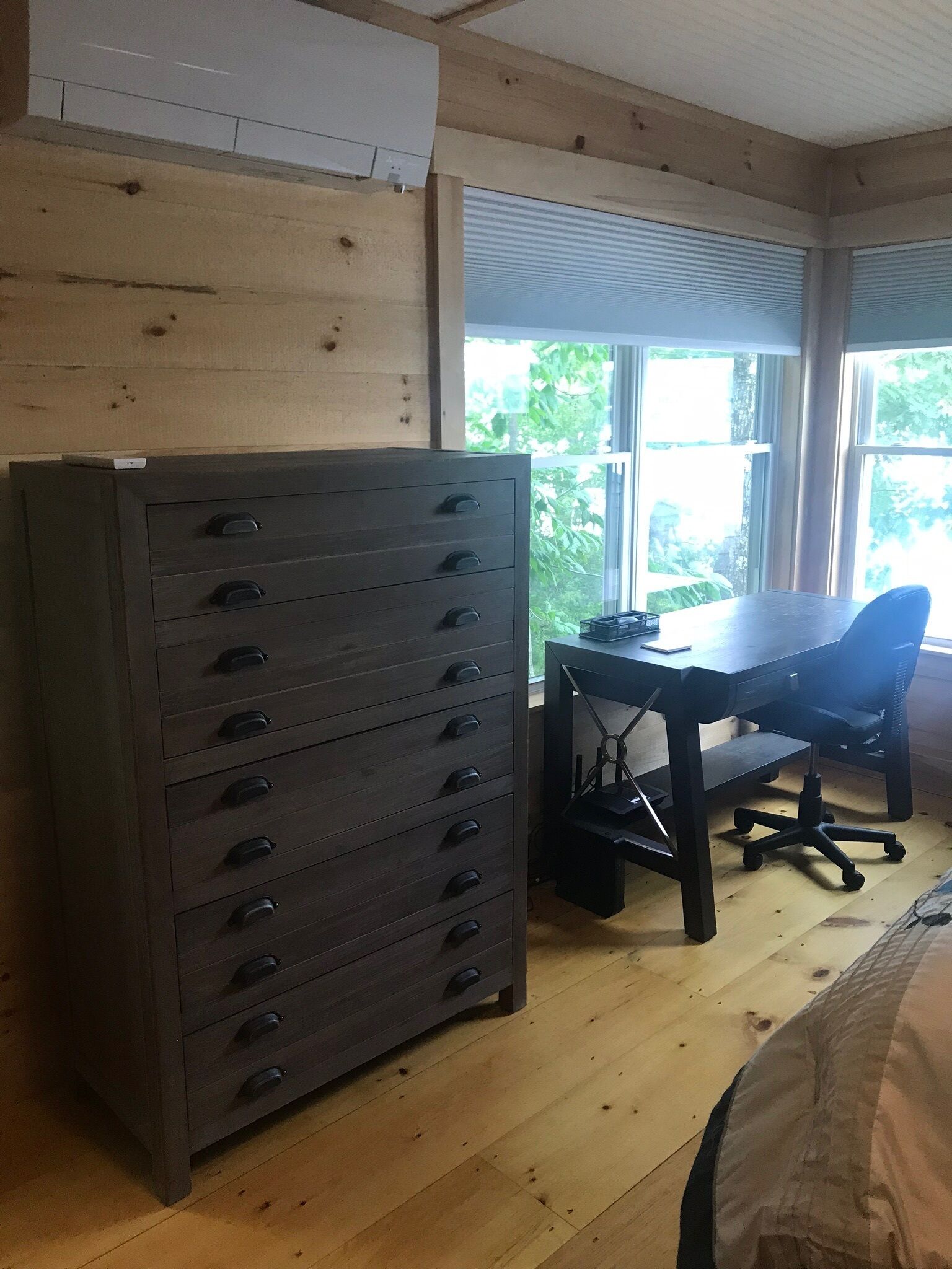 A room with a wooden dresser, a desk with a chair, and large windows.