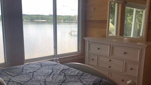 A bedroom with a large window, a bed with a patterned bedspread, a dresser, and a ceiling fan. - Lake Front Taylor Pond Cottage (Auburn)