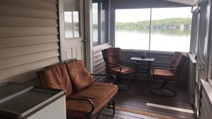 A covered porch with a brown leather sofa and two chairs, a small table, and a view of a lake. - Lake Front Taylor Pond Cottage (Auburn)
