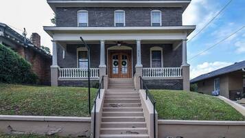 A two-story house with a front porch, a set of stairs leading to the entrance, and a brick facade.
