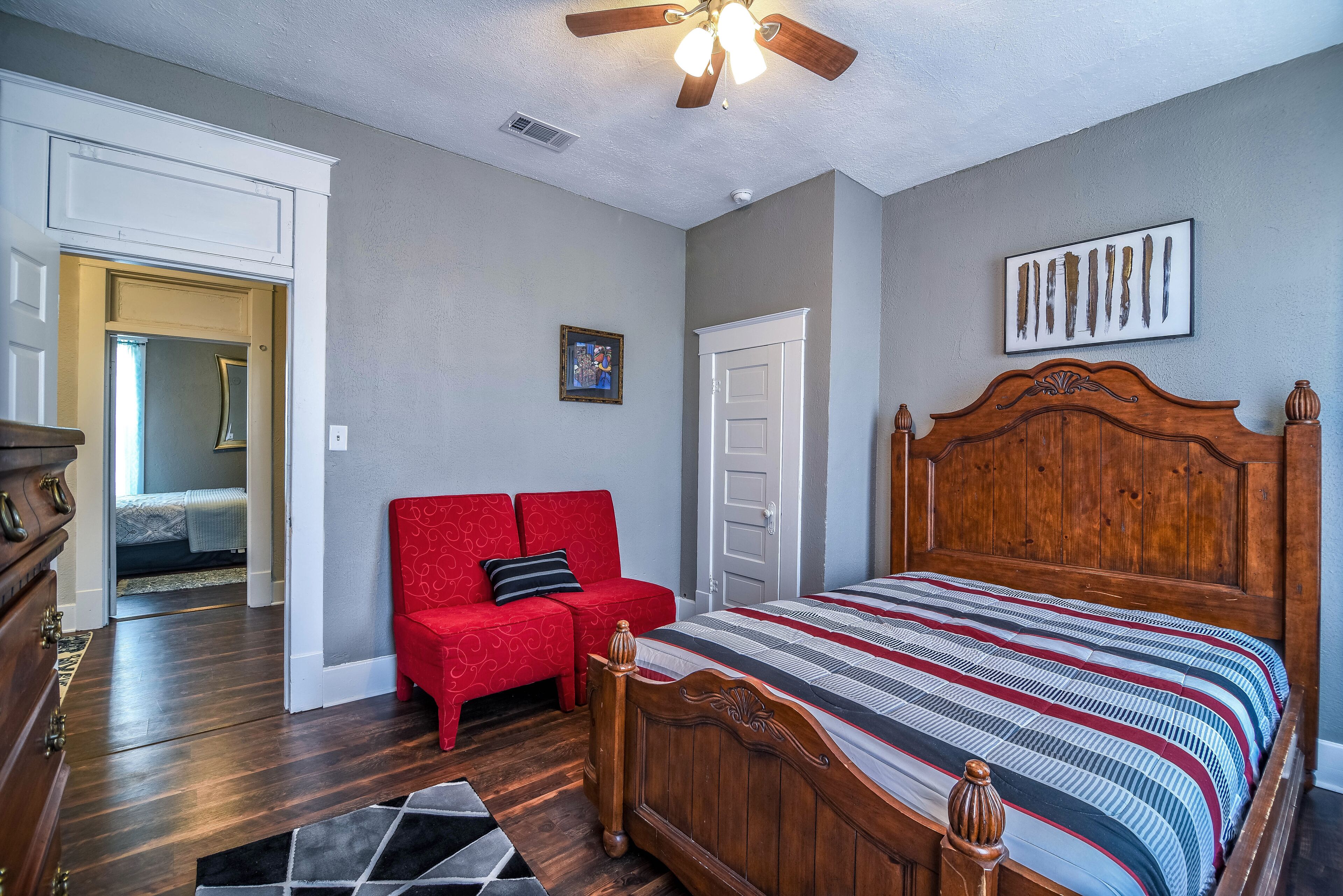 A bedroom with a wooden bed, a red sofa, a ceiling fan, and a framed picture on the wall.