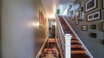Un couloir avec un escalier en bois, une moquette à motifs et des tableaux encadrés accrochés aux murs.