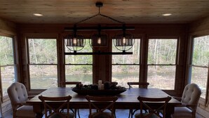 Un comedor con mesa y sillas de madera, ventanas amplias con vista al río y una araña.