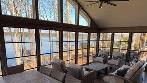 Ein Wintergarten mit großen Fenstern, Korbmöbeln und Blick auf einen See.