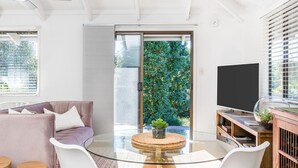 Un salon moderne avec une table en verre, un canapé, un téléviseur et une porte-fenêtre coulissante donnant sur un balcon agrémenté de plantes.