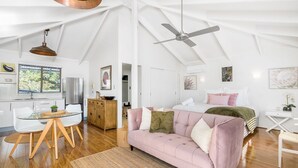 Un loft spacieux avec un plafond haut, un coin repas avec une table en verre, un canapé rose et un lit avec un plaid vert.