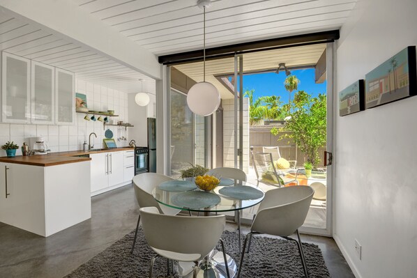 Enjoy meals at the glass-top dining table surrounded by white chairs and a large window offering a view of the outdoors.