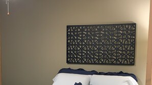 A neatly made bed with white and navy bedding, a decorative wall piece above it, and a patterned rug on the floor. - No Worries (Spiro)