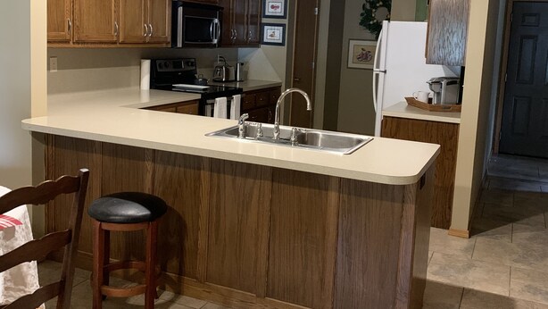 A kitchen with wooden cabinets, a stainless steel sink, and a built-in microwave. - No Worries (Spiro)