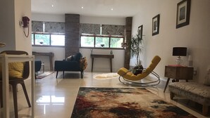 A spacious living room with a large window, a yellow rocking chair, a sofa, and a coffee table. - Luxury Private Apartment (Lincoln)