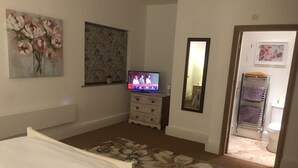 A bedroom with a bed, a television, a dresser, a mirror, and a bathroom visible through an open door. - Luxury Private Apartment (Lincoln)