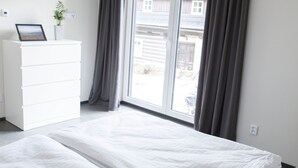 Een slaapkamer met een bed, een ladekast en een raam met gordijnen.