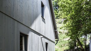 Een modern gebouw met een schuin dak, twee ramen en een stenen muur op de achtergrond.