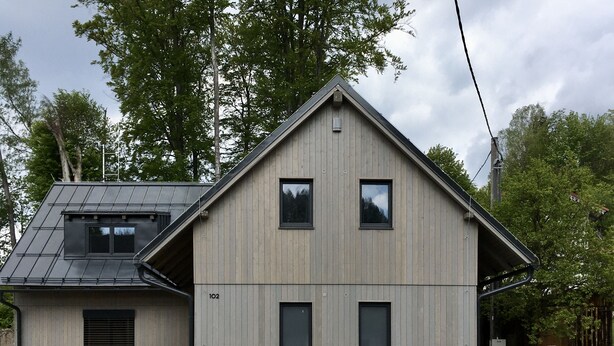 Een modern huis met twee verdiepingen, een schuin dak, een zichtbare zolder en het nummer '102' op de gevel.