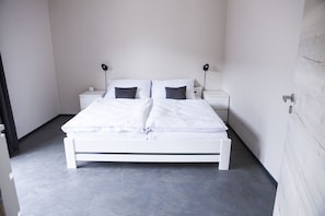 Un dormitorio minimalista con una cama blanca, dos mesitas de noche y una mesita auxiliar.