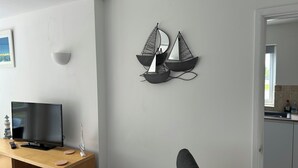 Moderni olohuone, jossa on litteänäyttöinen televisio, puinen mediakeskus ja seinälle kiinnitetty purjelaivamainen koriste.