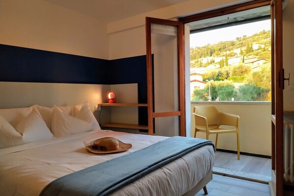 A bedroom with a bed, a nightstand, a window with a view of a hillside, and a chair by the window.