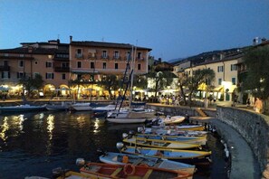 A waterfront area with boats docked along a stone quay, buildings with balconies, and a building with a sign that reads "ALBERGO GARDEN".