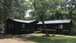 A rustic cabin with a metal roof, surrounded by dense trees and a gravel driveway. - Country River Cabin (Murphy)