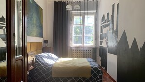 Een slaapkamer met een bed, nachtkastje, lamp, raam met gordijnen en een radiator.