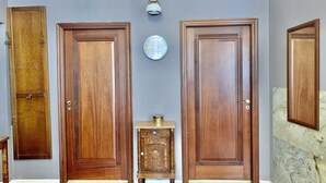 Een gang met twee houten deuren, een klein houten kastje en een klok aan de muur.