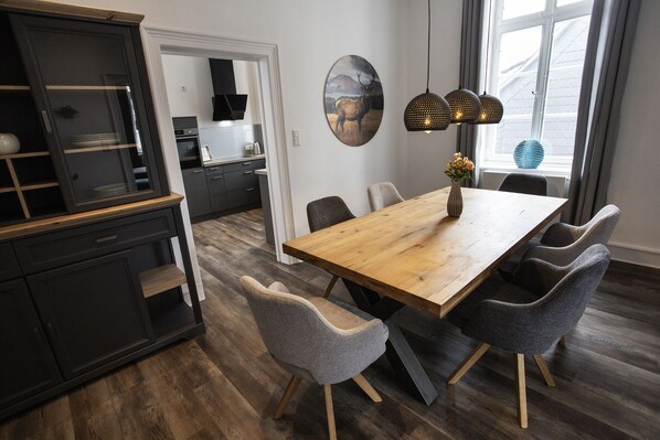 Une cuisine moderne avec des meubles de couleur sombre, une table à manger en bois et des chaises recouvertes d’un tissu gris.