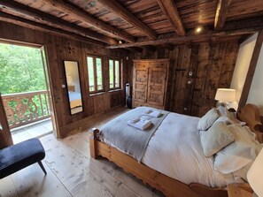 Ein Schlafzimmer aus Holz mit Bett, einer Bank, einem Balkon und Blick ins Grüne.