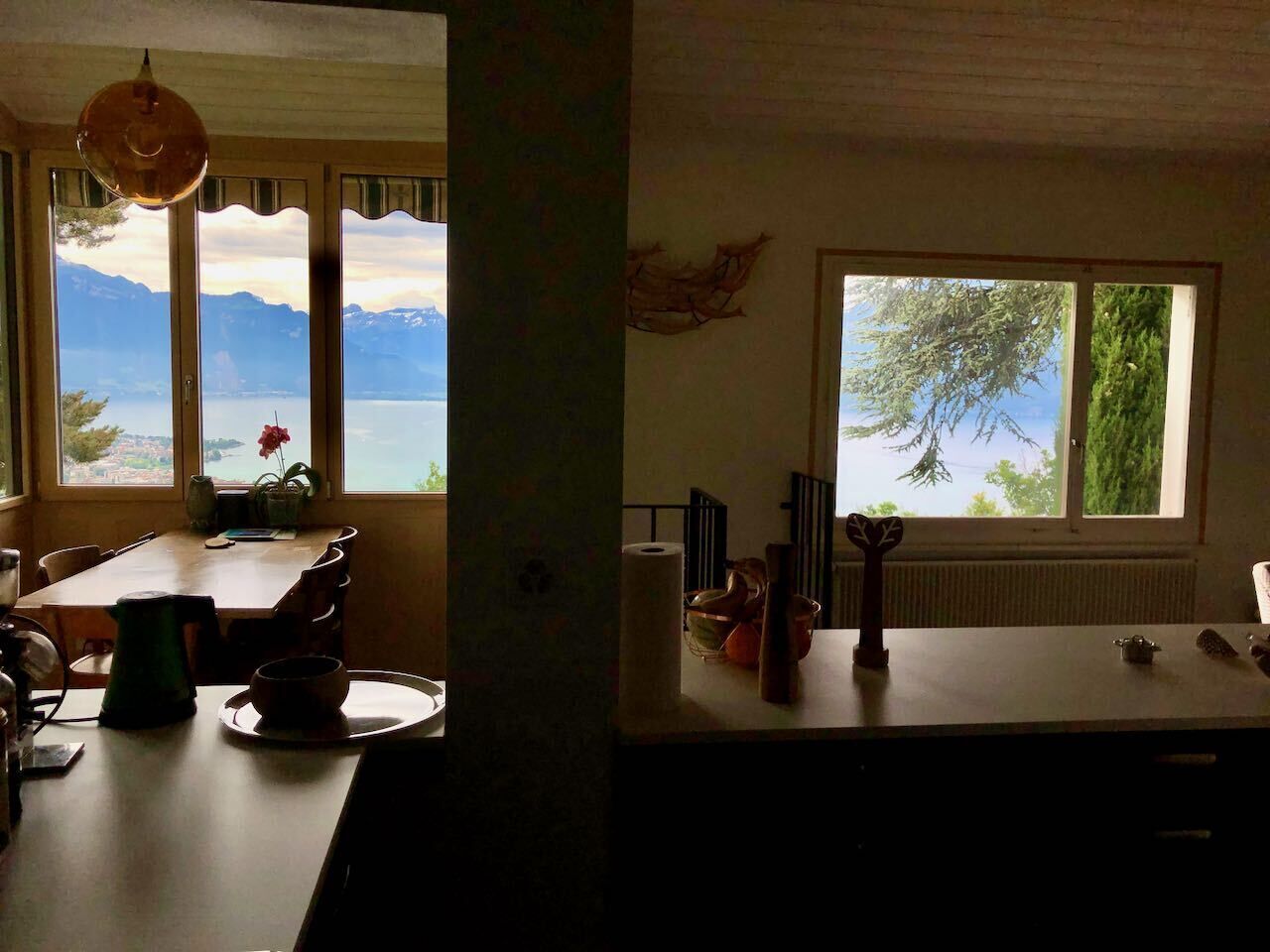 Une cuisine avec vue sur un lac et des montagnes, un coin repas avec une table et des chaises, et une fenêtre donnant sur les arbres.