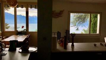 Une cuisine avec vue sur un lac et des montagnes, un coin repas avec une table et des chaises, et une fenêtre donnant sur les arbres.