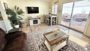 Een woonkamer met een bank, salontafel, televisie en uitzicht door een glazen deur op een terras.