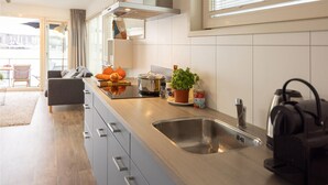 A modern kitchen with a stainless steel sink, a kettle, and a potted plant on the counter.