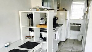 A compact kitchen with white cabinetry, a small dining area with a white table and chairs, and a tiled floor. - Petrina Apartments (Pompano Beach)