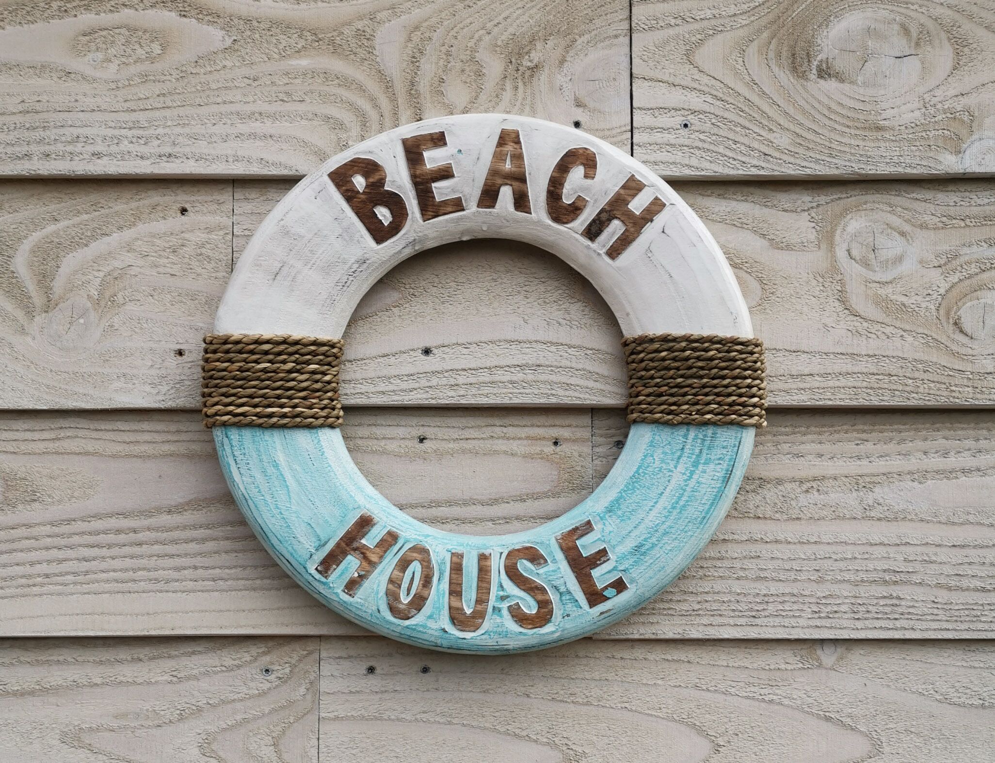 A circular sign with the words "BEACH HOUSE" on a wooden background.