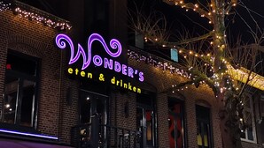 Un bâtiment en briques avec une enseigne au néon indiquant « Wonder's eten & drinken » et des guirlandes lumineuses.