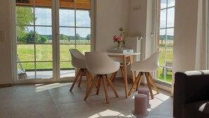 Une pièce spacieuse avec de grandes fenêtres, un coin repas avec des chaises et une table, et une vue sur l’extérieur.