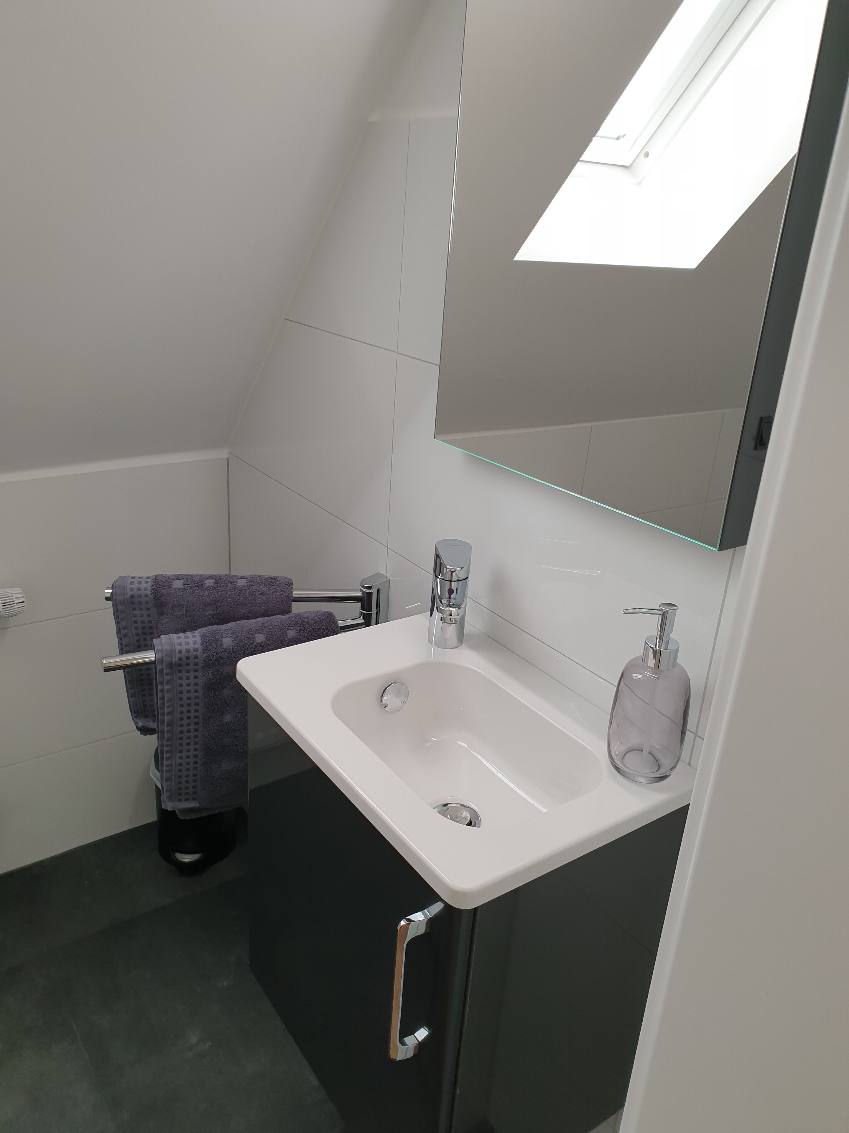 Ein modernes Badezimmer mit einem weißen Waschbecken, einem Spiegel und einem Handtuchhalter.