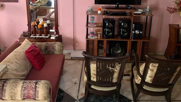 Ein Wohnzimmer mit einer Couch, Sesseln, einem Fernseher, einer Stereoanlage und einem Kronleuchter.