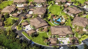 Eine Vogelperspektive zeigt ein Resort mit mehreren bungalowsartigen Gebäuden, einem zentralen Swimmingpool und gepflegten Grünflächen.
