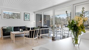 Una sala de estar moderna con un sofá, sillas, una mesa de comedor y un amplio ventanal con vistas a una terraza.