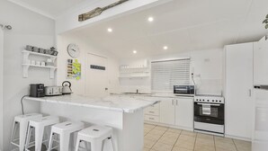 Una cocina moderna con armarios blancos, una isla de mármol con taburetes altos, horno empotrado y una ventana con persianas.