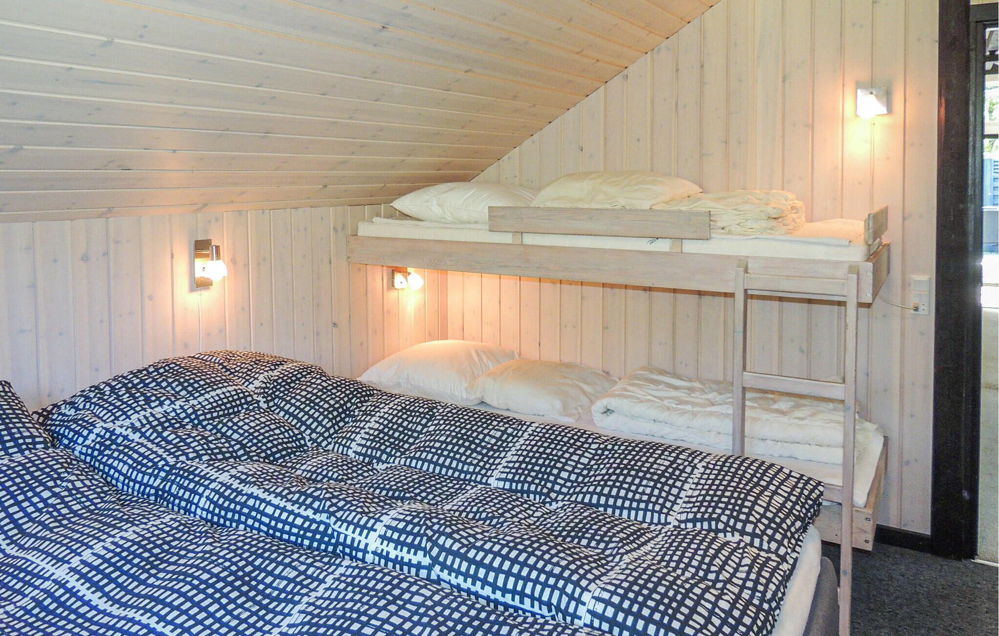 A bunk bed room with a checkered bedspread, wooden walls, and wall-mounted lights.