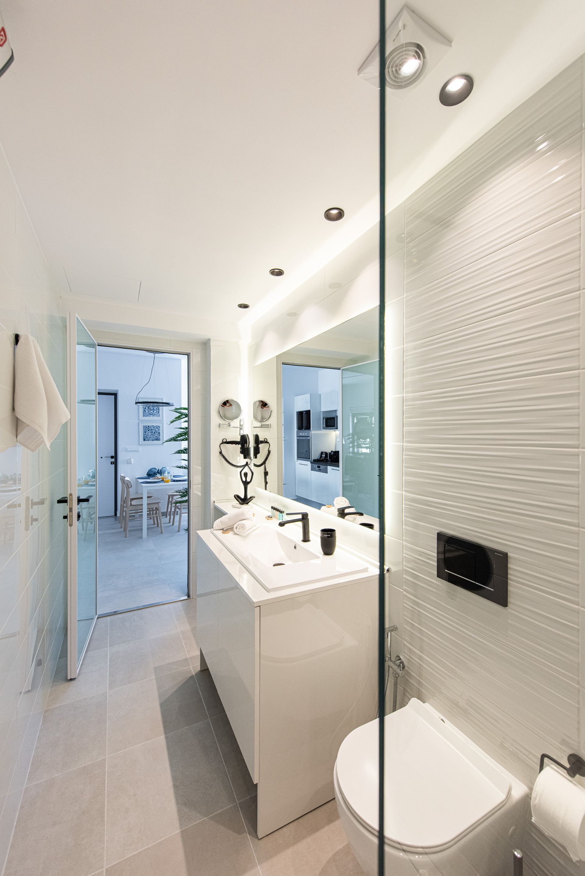 Un baño moderno con cabina de ducha de vidrio, un lavabo blanco con espejo y un inodoro.