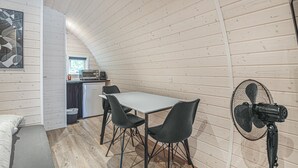Een compacte, knusse kamer met een eettafel en stoelen, een kitchenette en een ventilator.